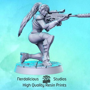 Peut inclure: Une figurine miniature grise et détaillée d'un personnage féminin agenouillé tenant un fusil. La figurine est posée dans une pose d'action dynamique, les cheveux du personnage flottant derrière elle. La figurine est posée sur une base circulaire.