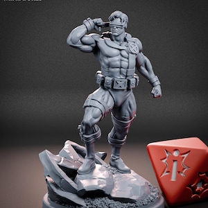 Può includere: Una miniatura in resina grigia di un personaggio muscoloso con visiera, cintura tattica con emblema a X e stivali, in piedi su una base rocciosa. Accanto alla figura c'è un dado rosso con un simbolo a forma di stella bianca e del testo.