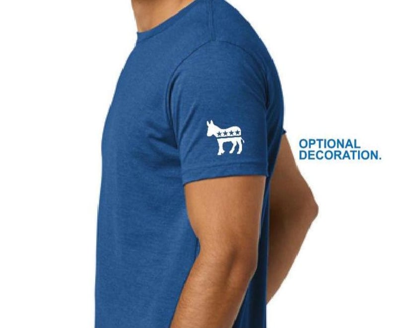 Puede incluir: Camiseta azul de manga corta con un dise&ntilde;o de burro blanco y estrellas en la manga izquierda. El texto "OPTIONAL DECORATION" est&aacute; a la derecha de la camiseta. La camiseta est&aacute; hecha de una tela suave y texturizada.
