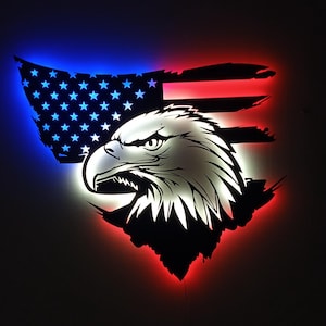 May include: A patriotic wall art piece featuring a stylized bald eagle head and an American flag design. The flag has red, white, and blue LED lighting. The eagle is white with black accents.