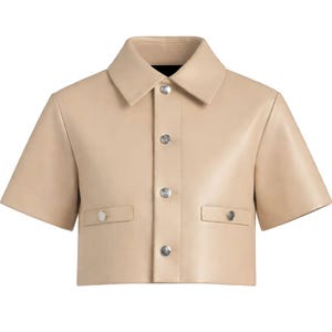 May include: A cropped, short-sleeved jacket in a light tan color. The jacket features a collared neckline, silver buttons, and two small pockets. The material appears to be leather or a leather-like fabric.