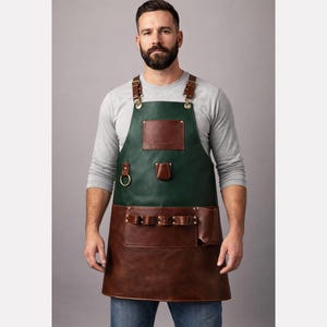 May include: A two-tone leather apron with a dark green upper section and a brown lower section. The apron has multiple pockets, a leather chest patch, and adjustable straps. It features a brass ring and rivets.