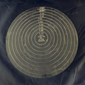 Könnte beinhalten: Eine schwarze Kreisschablone mit konzentrischen Kreisen, die Außendurchmesser von 5,08 cm bis 27,94 cm angeben. Der Text "CIRCLE TEMPLATES" und "OUTSIDE DIAMETER" sind ebenfalls sichtbar.
