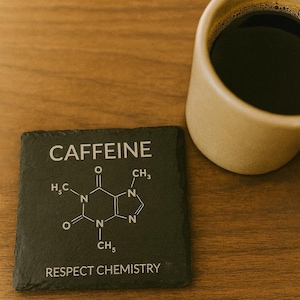 Könnte beinhalten: Ein quadratischer, schwarzer Schieferuntersetzer mit dem Wort "CAFFEINE" und der chemischen Struktur von Koffein in Weiß. Darunter steht der Text "RESPECT CHEMISTRY". Rechts befindet sich eine beige Tasse mit dunkler Flüssigkeit.