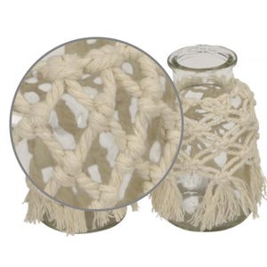 May include: A clear glass vase wrapped in a cream-coloured macrame cord featuring a knotted diamond pattern and a fringed bottom edge. The design includes a circular inset detail that highlights the intricate texture of the woven cotton rope.