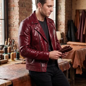 May include: A deep red motorcycle jacket with a textured snakeskin pattern, featuring a notched lapel, silver-tone metal zips, and long sleeves. The jacket is worn over a plain black t-shirt and paired with black trousers.
