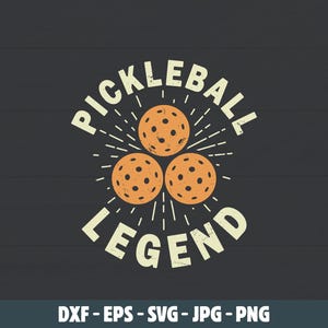 Peut inclure: Conception graphique sur fond gris foncé avec les mots "PICKLEBALL LEGEND" en police vintage. Trois balles de pickleball oranges sont centrées au-dessus du mot "LEGEND". Le design comprend des lignes rayonnantes.