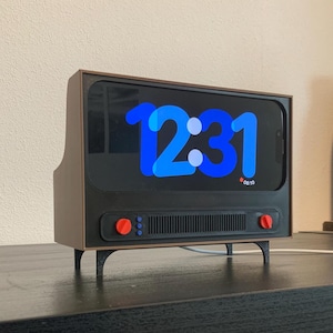 May include: A retro-style digital clock with a brown frame and black screen displaying the time 12:31 in blue. The clock has red buttons and a speaker grill. It is elevated on small black legs.