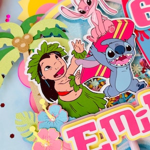 K&ouml;nnte beinhalten: Ein farbenfroher Tortenaufsatz mit den Zeichentrickfiguren Lilo, Stitch und Angel. Das Design umfasst einen rosa und gelben Namen, Palmen, Hibiskusbl&uuml;ten und eine Sonne. Der Aufsatz ist mit Glitzer und Konfetti verziert.