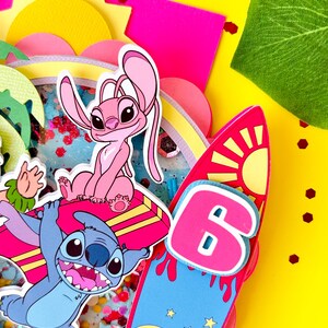 K&ouml;nnte beinhalten: Ein farbenfrohes Papierkunstwerk mit den Zeichentrickfiguren Stitch und Angel, einem Surfbrett mit der Zahl 6 und einer gelben Sonne. Der Hintergrund ist gelb mit rosa und gr&uuml;nen Akzenten und Konfetti.