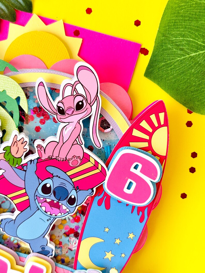 K&ouml;nnte beinhalten: Ein farbenfrohes Papierkunstwerk mit den Zeichentrickfiguren Stitch und Angel, einem Surfbrett mit der Zahl 6 und einer gelben Sonne. Der Hintergrund ist gelb mit rosa und gr&uuml;nen Akzenten und Konfetti.