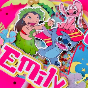 K&ouml;nnte beinhalten: Ein lebendiger Tortenaufsatz mit Figuren aus dem Animationsfilm Lilo & Stitch. Das Design umfasst den Namen "Emily" in Pink und Gelb sowie Bilder von Stitch, Lilo und Angel, vor einem hellrosa Hintergrund mit tropischen Akzenten.