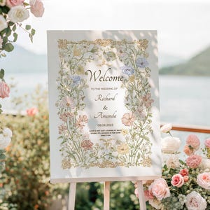 May include: A wedding welcome sign on an easel, featuring floral artwork and the names Richard & Amanda. The sign is surrounded by flowers in shades of pink, white, and yellow. The text reads "Welcome" and the wedding date.