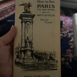 May include: A vintage travel brochure for motor tours of Paris and its environs, featuring a black and white illustration of the Arc de Triomphe, with the text "How to See Paris, Its Environs and the Battlefields, Motor Tours, Thos. Cook & Son, 1926, Paris."