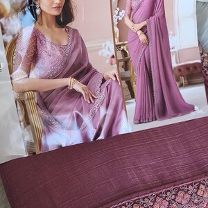May include: A mauve-colored saree with intricate embroidery and sequin detailing. The saree features a matching blouse with embellished sleeves. The image shows a woman wearing the saree, showcasing its elegant drape and design.