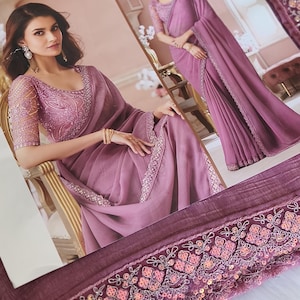 May include: A mauve saree with intricate embroidery and sequin detailing. The saree features a sheer, embellished bodice and sleeves. The border is adorned with floral and geometric patterns. The image shows two women wearing the saree.