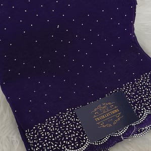 May include: A dark purple fabric adorned with small silver studs. The lower edge is decorated with a detailed border of silver beads and a scalloped trim. A navy blue tag with gold text reads "TN COLLECTIONS LTD".