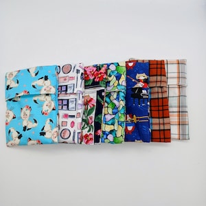 Puede incluir: Una colección de bolsas de tela con varios diseños. Los diseños incluyen gatos, maquillaje, flores, vidrieras, instrumentos musicales, cuadros escoceses y un diseño de cuadros blancos y naranjas. Las bolsas están dobladas en la parte superior.