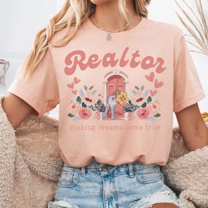 May include: A pink t-shirt with the text "Realtor" in a retro font, a pink door with keys and a house key chain, and floral accents. The text "making dreams come true" is below the image.