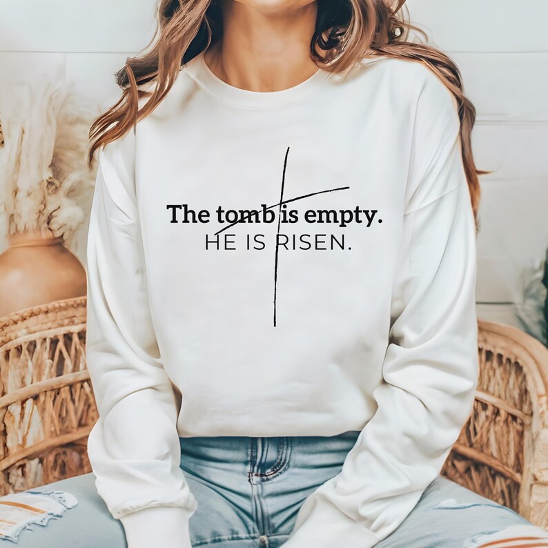 May include: White long-sleeve sweatshirt with a black cross and the text "The tomb is empty. HE IS RISEN."