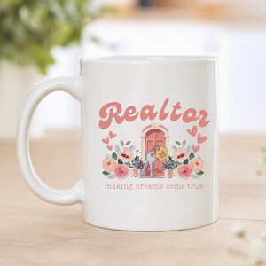May include: White ceramic mug with a pink and yellow design. The mug says "Realtor making dreams come true" with a pink door and keys.