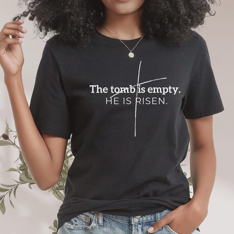 May include: Black t-shirt with white text that reads "The tomb is empty. HE IS RISEN." A white cross is drawn behind the text.
