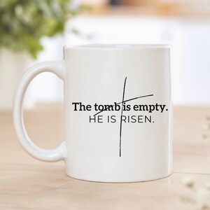 May include: White ceramic coffee mug with a black cross and the text "The tomb is empty. HE IS RISEN."
