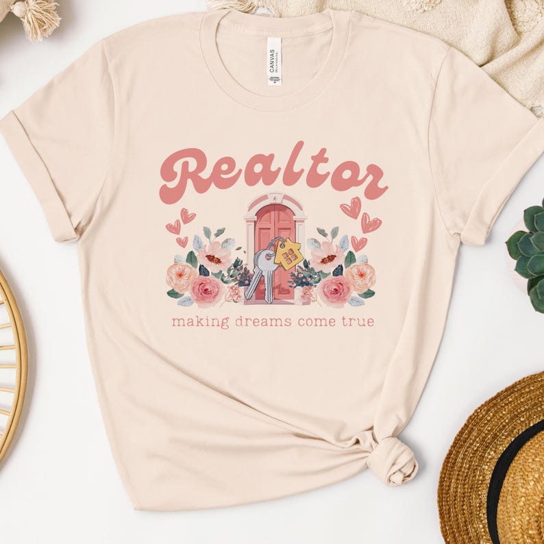 May include: A beige t-shirt with a pink graphic of a house with a key and the text "Realtor making dreams come true".