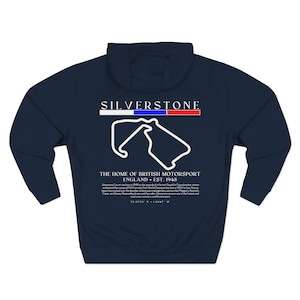 May include: A navy blue hooded sweatshirt featuring a white graphic of the Silverstone circuit track layout on the back. The design includes the text SILVERSTONE, THE HOME OF BRITISH MOTORSPORT, ENGLAND EST. 1948, and a paragraph of historical text.