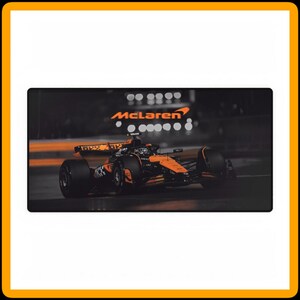 以下が含まれることがあります： 黒とオレンジ色のマクラーレンF1レーシングカーが黒い面にあります。車は動いており、オレンジ色のマクラーレンのロゴが見えます。背景は暗く、ぼやけた光があります。
