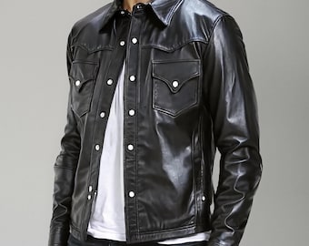Puede incluir: Una chaqueta de cuero negro con cuello en punta, mangas largas y cierre frontal de botones con broches de metal plateado. La chaqueta incluye dos bolsillos en el pecho con solapas en punta y broches, usada sobre una camiseta blanca lisa.