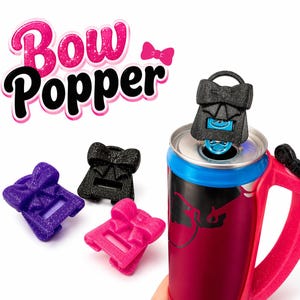 May include: The image shows a Bow Popper, a bow-shaped can opener, in black, purple, and pink. The Bow Popper is on top of a red and black can with a blue rim. The text "Bow Popper" is in pink and black.