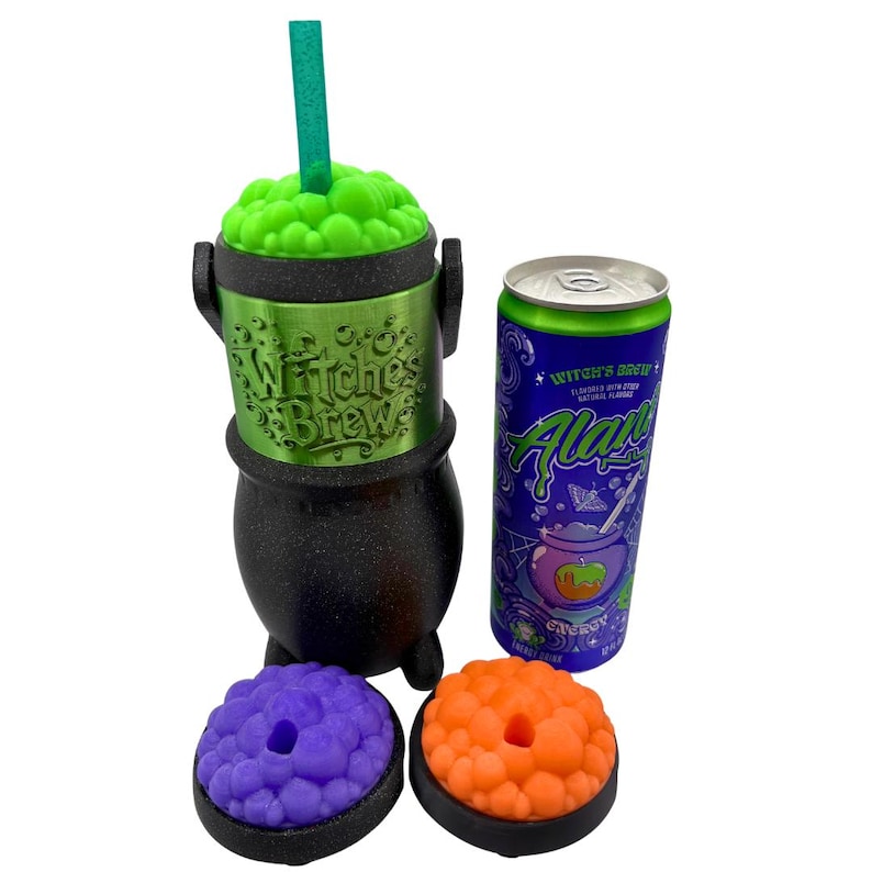 May include: A black cauldron-shaped cup with a green textured lid and a green straw, featuring the embossed text "Witch's Brew". Beside it sits a purple and green "Witch's Brew" energy drink can, along with two additional cauldron lids in purple and orange.