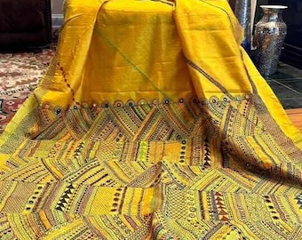 May include: A vibrant yellow textile with intricate geometric patterns and decorative trim. The fabric is draped over a chair, showcasing the detailed embroidery and colorful accents. The design incorporates various shapes and lines, creating a visually rich composition.