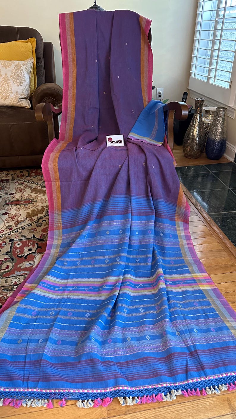 Pu&ograve; includere: Un tessuto vibrante con una tavolozza di colori viola, blu, rosa e giallo. Il tessuto &egrave; drappeggiato su una sedia, mostrando un motivo a righe con dettagli a diamante. I bordi sono rifiniti con nappe. Il tessuto ha il marchio "SPARSH" su un'etichetta.
