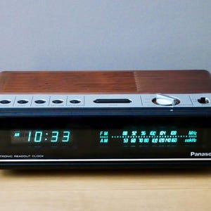 Könnte beinhalten: Ein elektronischer Panasonic Radiowecker mit einer Oberseite in Holzoptik und einer schwarzen Frontblende. Das Display zeigt die Uhrzeit 10:33 in grünen Digitalzahlen neben einer analogen Radiofrequenz-Skala für FM- und AM-Bänder mit grünem Text.