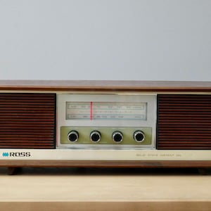 Puede incluir: Radio vintage Ross Solid State Portrait con una carcasa de madera y una cara plateada. La radio tiene rejillas de altavoz marrón oscuro y un dial de sintonización central. Tiene cuatro perillas verdes y el texto "ROSS" y "SOLID STATE PORTRAIT" en el frente.