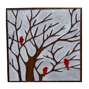 Könnte beinhalten: Ein quadratisches String-Art-Stück mit einem Baum mit weißen Fadenblättern und braunen Ästen. Drei rote Vögel sitzen auf den Ästen. Das Kunstwerk ist in einem dunkelbraunen Holzrahmen gerahmt.