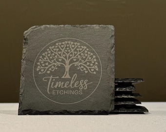 May include: A set of six black slate coasters with a tree of life design and the text "Timeless Etchings".