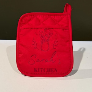 May include: Red quilted oven mitt with a personalized design. The design features a black silhouette of a pot with utensils inside, surrounded by leaves. The text "Sarah's Kitchen" is embroidered below the design.