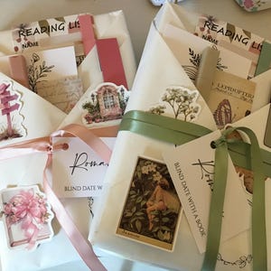 May include: Two white gift-wrapped packages with green and pink ribbons. The packages are decorated with stickers and tags. The text on the tags reads "Roma" and "Blind Date With A Book".