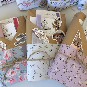 May include: Three brown paper wrapped journals with floral patterned paper on the front. Each journal has a sticker with the text "Reading Log" and a small butterfly graphic. The journals are tied with twine.