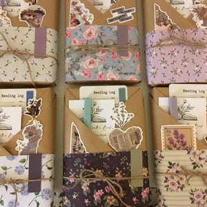 May include: Three brown paper-wrapped journals with floral patterned paper covers. Each journal has a different floral pattern and includes a variety of decorative stickers and embellishments. The journals are labeled "Reading Log".