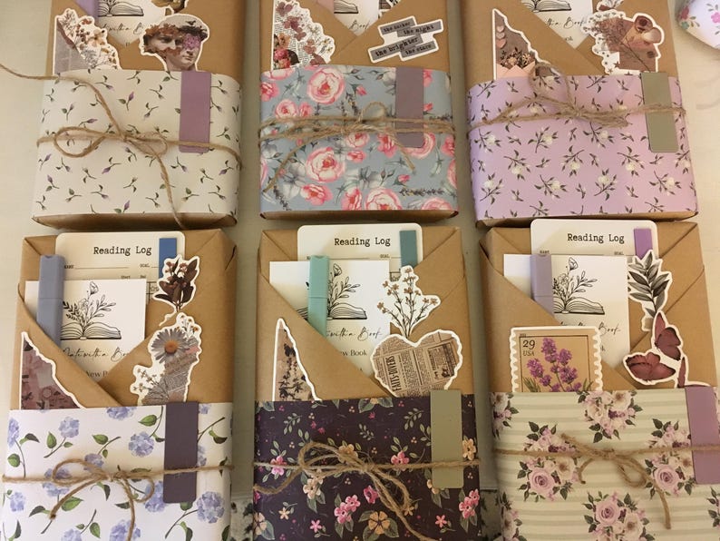 May include: Three brown paper-wrapped journals with floral patterned paper covers. Each journal has a different floral pattern and includes a variety of decorative stickers and embellishments. The journals are labeled "Reading Log".