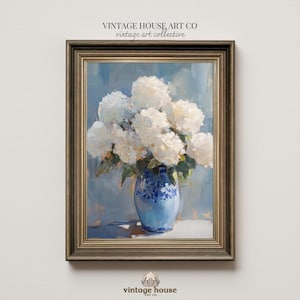Puede incluir: Pintura al óleo enmarcada de hortensias blancas en un jarrón azul y blanco. El jarrón está sobre una superficie blanca sobre un fondo azul. El marco es dorado. El texto "VINTAGE HOUSE ART CO vintage art collective" está en la parte superior.
