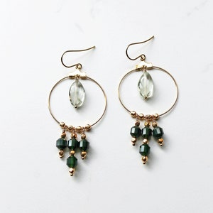 Chandelier earrings that have a main circle, within the circle is a smooth oval peridot gemstone. Hanging from the circle are  green prism cut agate gemstones with gold beads.