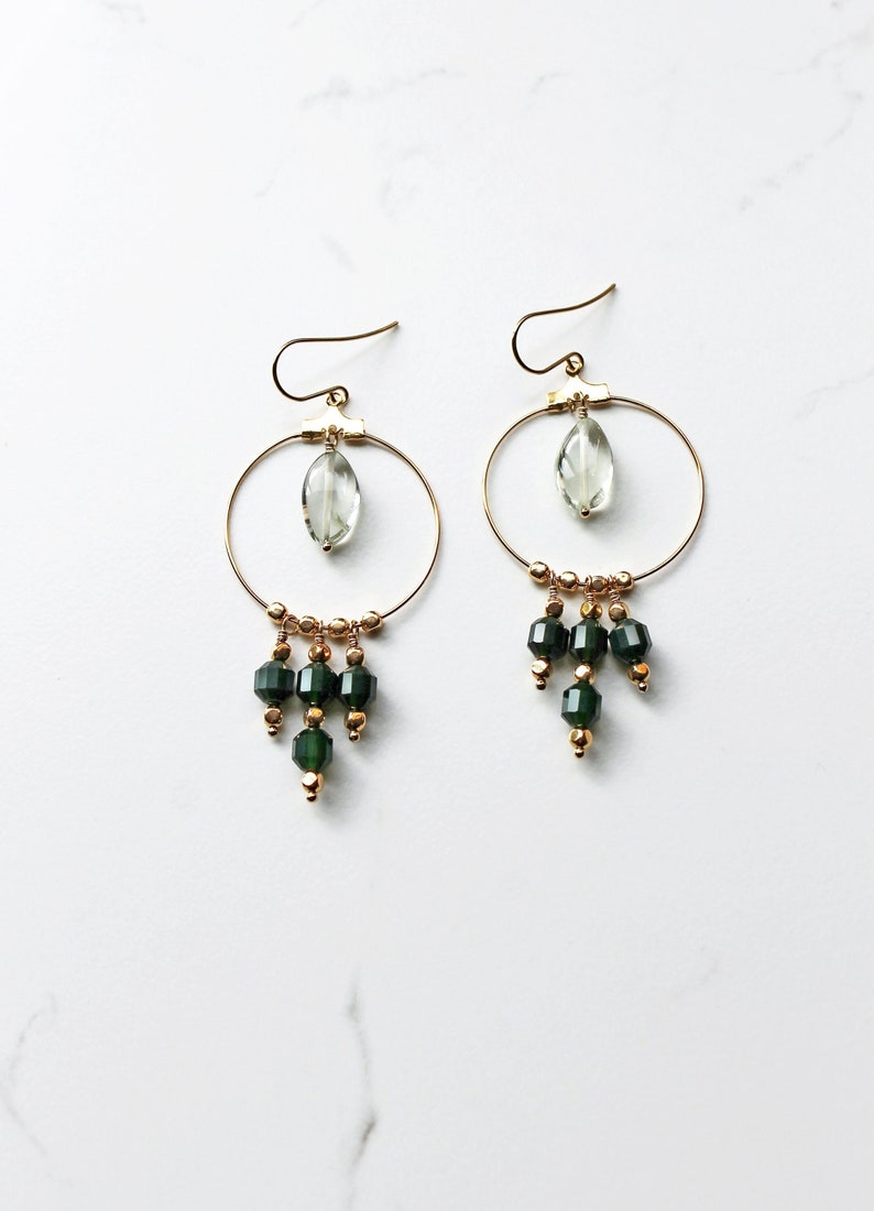 Chandelier earrings that have a main circle, within the circle is a smooth oval peridot gemstone. Hanging from the circle are  green prism cut agate gemstones with gold beads.
