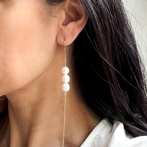 May include: A pair of long, gold chain earrings with three white pearls hanging from each chain.