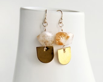 May include: A pair of gold earrings with a teardrop-shaped gold charm and a raw, natural citrine stone.