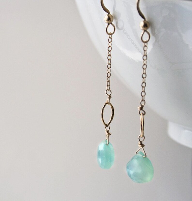 Pu&ograve; includere: Un paio di orecchini pendenti in oro con una pietra preziosa blu chiaro e un ciondolo ovale in oro.